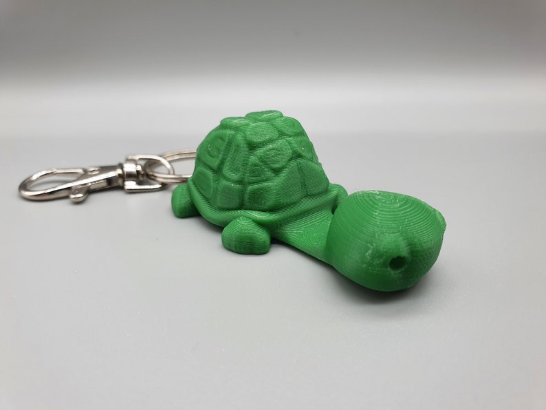 May include: A green plastic turtle keychain with a silver key ring. The turtle has a detailed shell and a long neck.