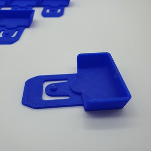 May include: A close-up of several bright blue plastic clips. One clip is in focus, showing a rectangular container shape with a curved handle and a circular hole. The other clips are slightly out of focus in the background.