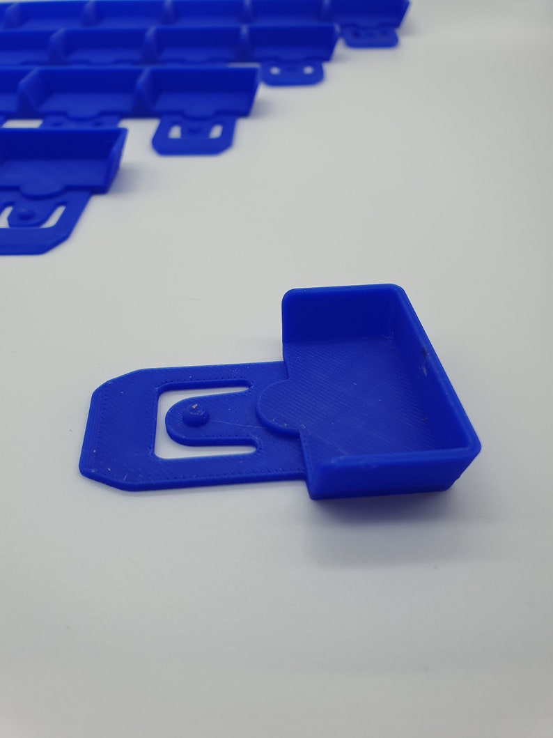 May include: A close-up of several bright blue plastic clips. One clip is in focus, showing a rectangular container shape with a curved handle and a circular hole. The other clips are slightly out of focus in the background.
