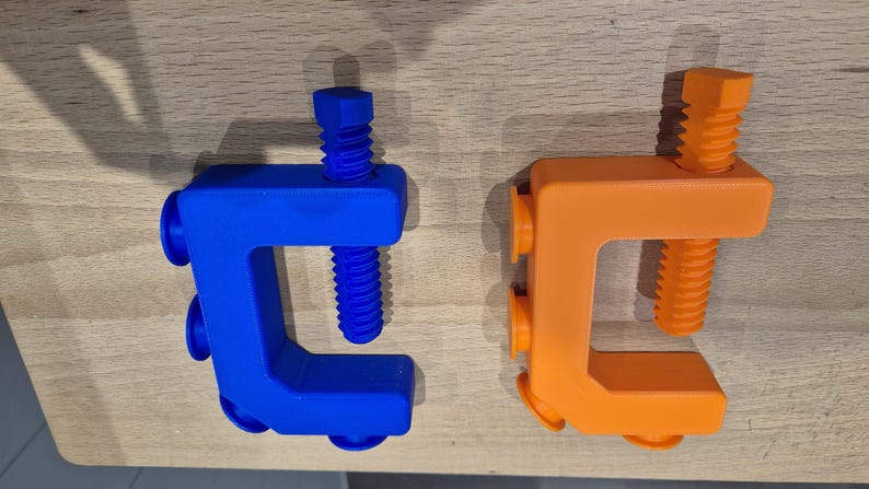 May include: Two plastic clamps, one blue and one orange, with a screw-like design. The clamps are made of a soft, flexible material and have a rounded shape.