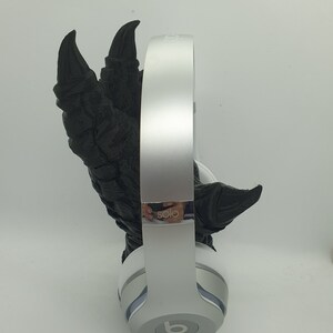 May include: White Beats by Dre Solo headphones with a black, 3D printed, dinosaur claw holding the headphones.