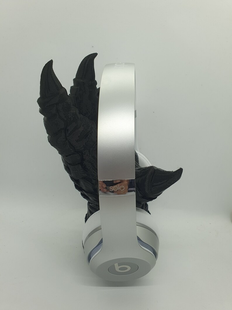 May include: White Beats by Dre Solo headphones with a black, 3D printed, dinosaur claw holding the headphones.
