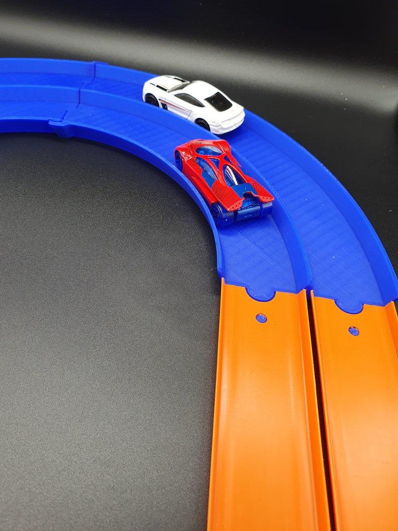 May include: A blue and orange Hot Wheels track set with two toy cars. One car is red and the other is white.