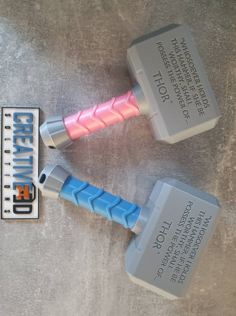 May include: Two 3D printed toy hammers with a gray head and a handle. One handle is pink and the other is blue. The hammers have the inscription "WHOSOEVER HOLDS THIS HAMMER, IF SHE BE WORTHY, SHALL POSSESS THE POWER OF... THOR" on the gray head.