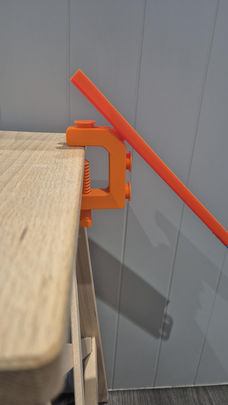 May include: An orange plastic clamp attached to a wooden surface, holding a bright orange plastic track piece.