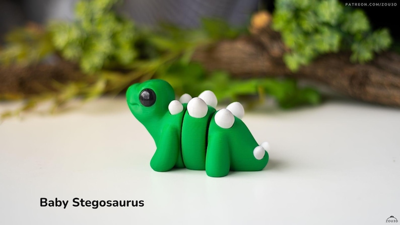 May include: A small, green, hand-painted baby stegosaurus figurine with white plates on its back. The figurine has large, black eyes and a cute, cartoonish expression.