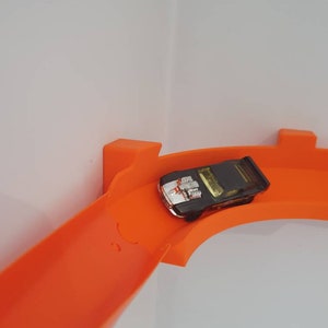 May include: A black toy car with a silver stripe races down an orange plastic track.