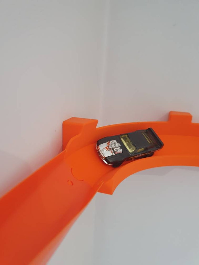 May include: A black toy car with a silver stripe races down an orange plastic track.