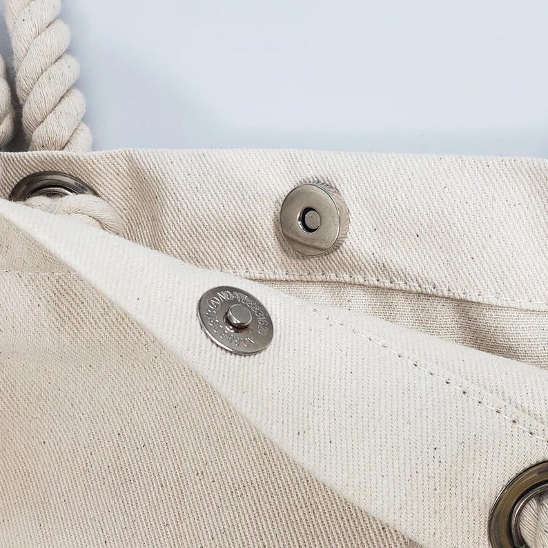a close-up view of a beige fabric, possibly a piece of clothing or a bag, with a metal button visible.