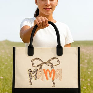 A woman holding a large tote bag with the word "Mama" printed on it.