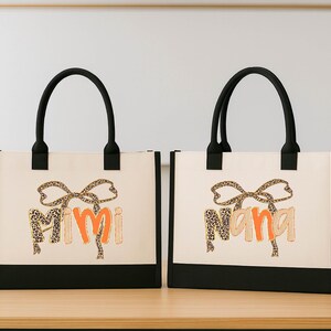 Two black tote bags with the word "Mimi" printed on them, placed on a wooden surface.