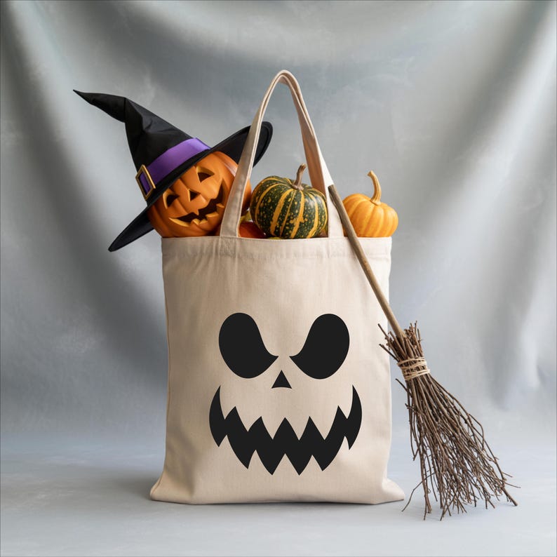A Halloween-themed tote bag with a carved jack-o-lantern and a broom, along with a small pumpkin and gourds, are displayed against a gray background.