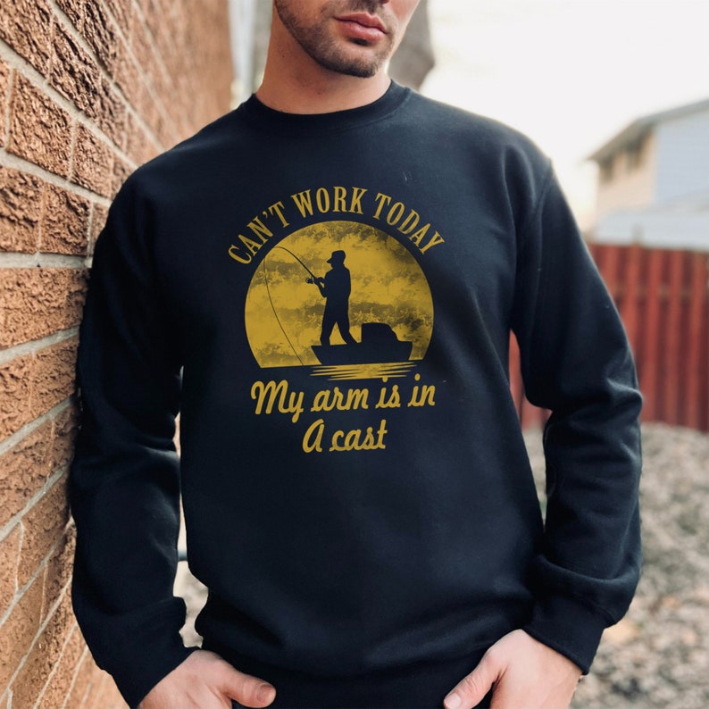 May include: Black sweatshirt with a yellow graphic of a person fishing in a boat with the text "Can't work today, my arm is in a cast."