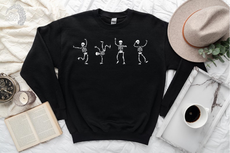 Puede incluir: Sudadera negra con un gr&aacute;fico blanco de cuatro esqueletos bailando. Los esqueletos est&aacute;n en varias poses, con los brazos y las piernas extendidos. La sudadera est&aacute; hecha de un material suave.
