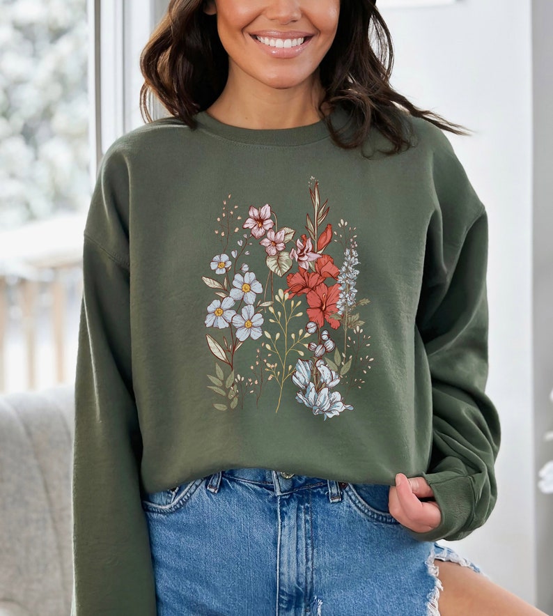 Pu&ograve; includere: Una felpa verde con una stampa floreale con fiori rosa, rossi, blu e bianchi. La felpa ha maniche lunghe e un collo rotondo.