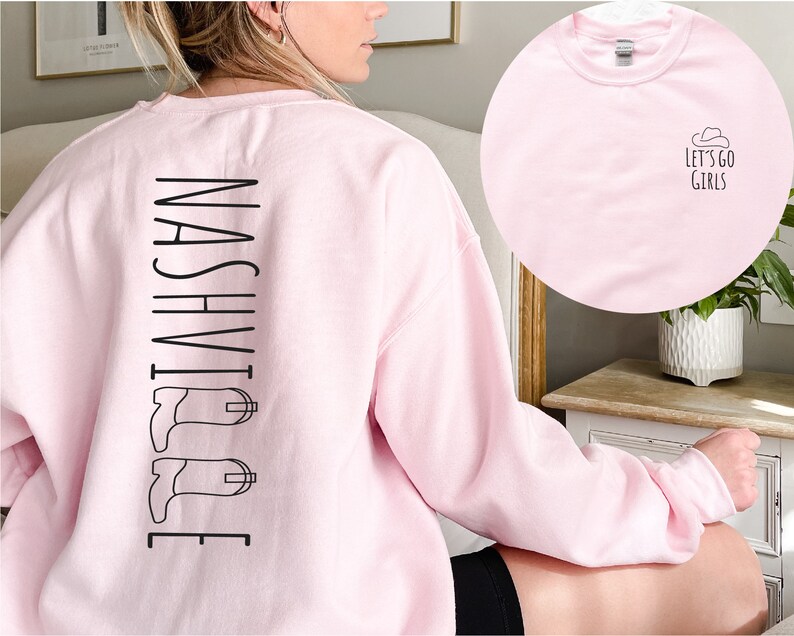 May include: Pink sweatshirt with the word "NASHVILLE" printed vertically down the back, with a pair of black cowboy boots on either side of the word. The front of the sweatshirt is plain pink.