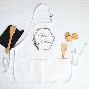 May include: White kitchen apron with a black geometric design and the text "Rose's Kitchen".
