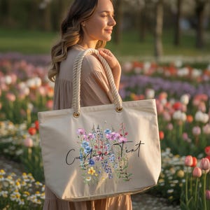 A woman is standing in a field of colorful flowers, holding a large tote bag with a floral design.