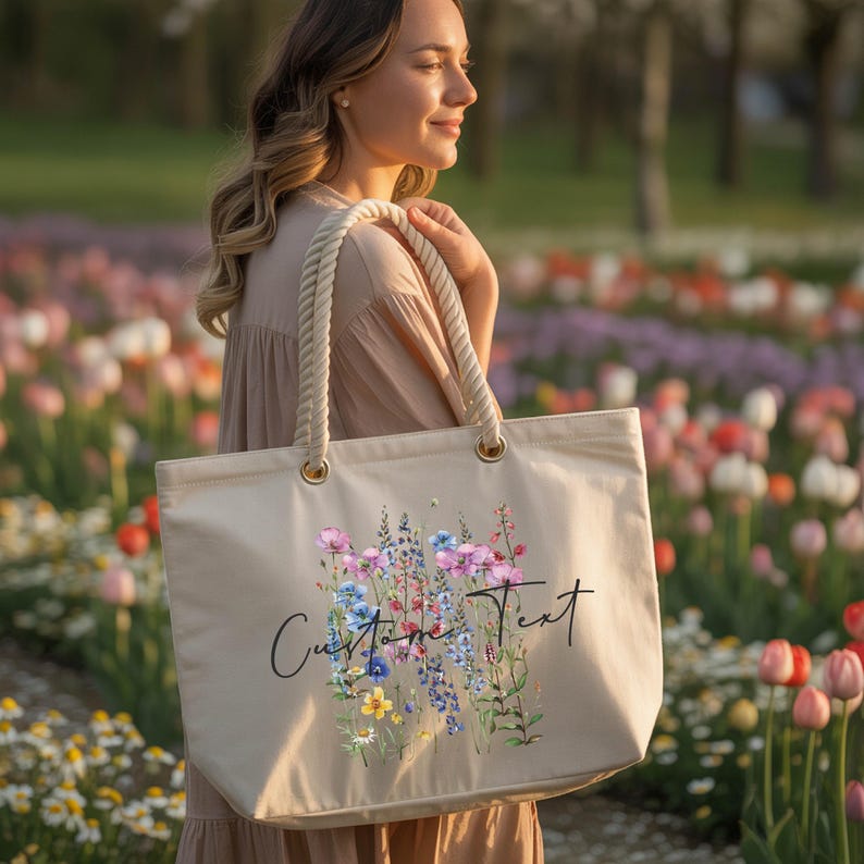 A woman is standing in a field of colorful flowers, holding a large tote bag with a floral design.