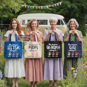 Four women standing in a row, each holding a tote bag with a handprint design, smiling and posing for a photo.