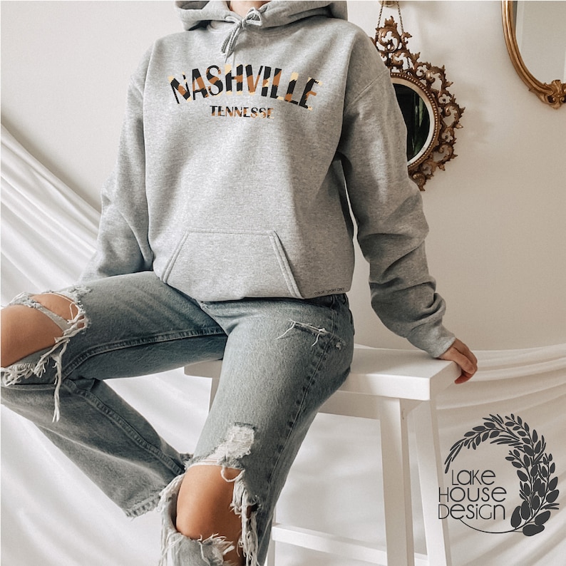 May include: A gray hooded sweatshirt with the text "Nashville Tennessee" in a yellow and brown patterned font.