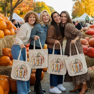 May include: Four women smiling and holding canvas tote bags with pumpkin designs. Each bag has a different name printed on it: Jennifer, Grace, Emily, and Julia. The bags feature a pumpkin design with orange, yellow, and brown colors.