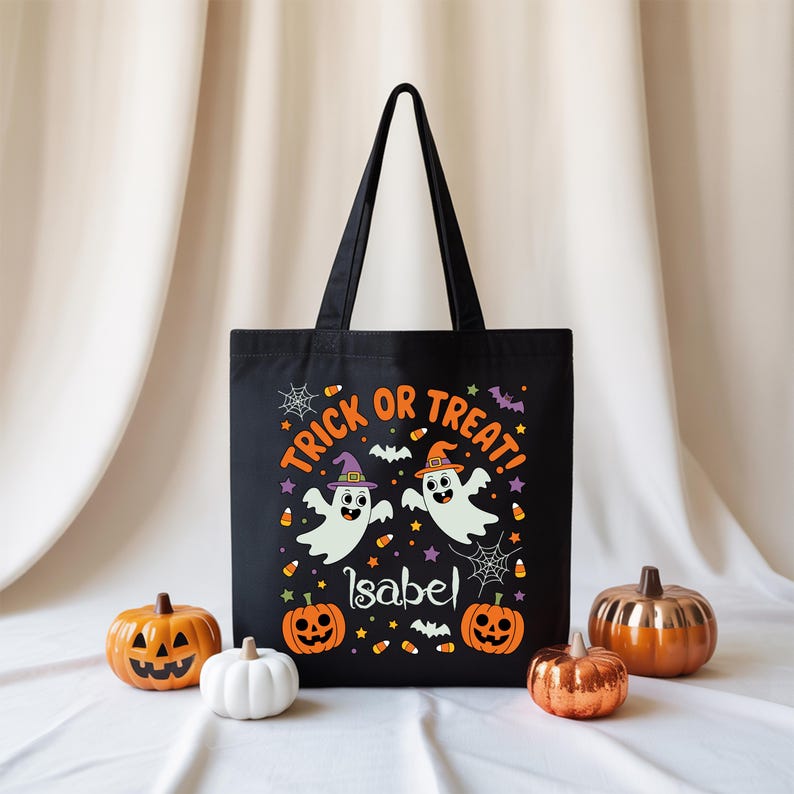 May include: Black Halloween tote bag with the words "Trick or Treat!" and the name "Isabel". The bag features two cartoon ghosts wearing witch and wizard hats, surrounded by pumpkins, bats, and candy corn.
