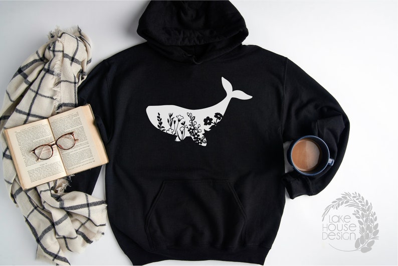 May include: Black hoodie with a white whale silhouette filled with floral designs. The hoodie has a drawstring hood and a kangaroo pocket.