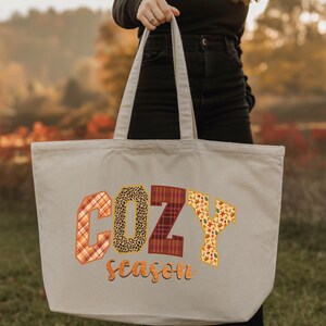 A person is holding a large tote bag with the word "COZY" printed on it, which appears to be a seasonal design.