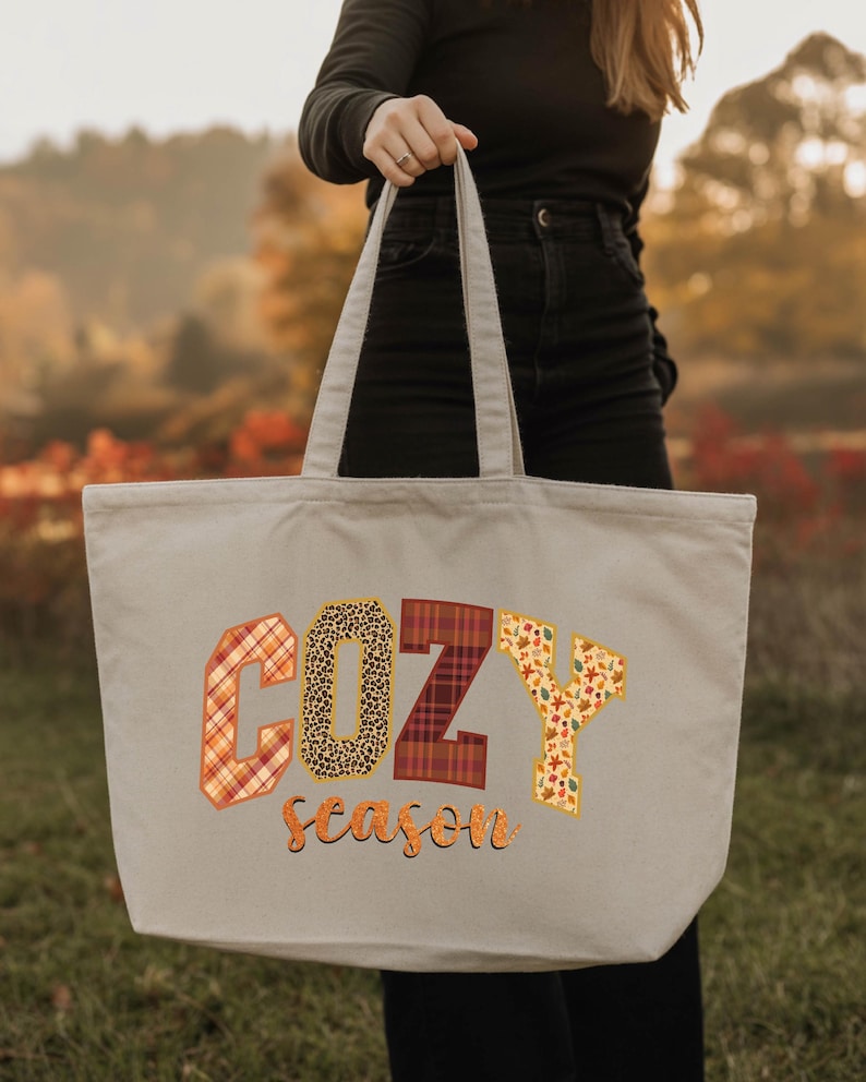 A person is holding a large tote bag with the word "COZY" printed on it, which appears to be a seasonal design.