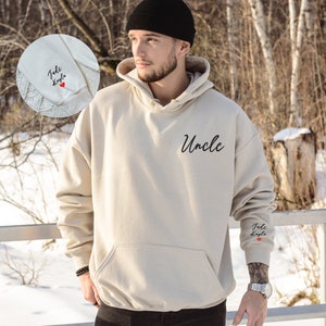 May include: A beige hoodie with the word "Uncle" printed on the front and the words "Jude Kayla" with a red heart printed on the left sleeve.