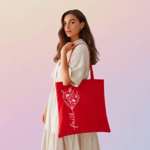A woman in a white dress holding a red tote bag with the word "faith" printed on it.