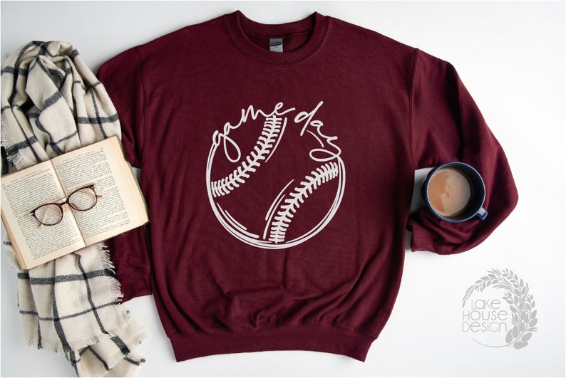 May include: A maroon sweatshirt with a white baseball graphic and the text "game day" in a handwritten font.