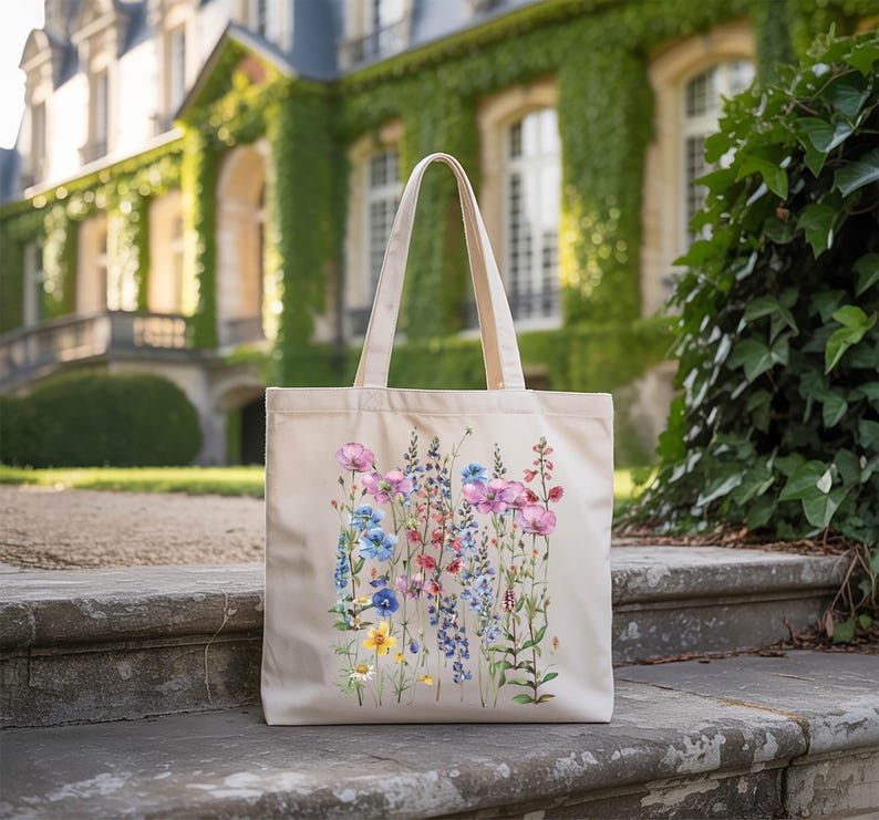 A beige tote bag with a floral design is placed on a stone step in front of a building with ivy growing on it.