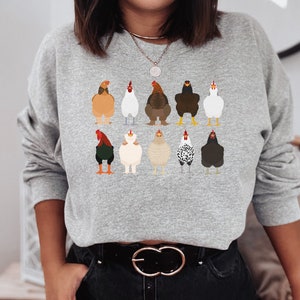 May include: A gray sweatshirt with a graphic print of 10 chickens in different colors and poses. The chickens are all facing forward and have their wings tucked in. The sweatshirt has long sleeves and a crew neck.
