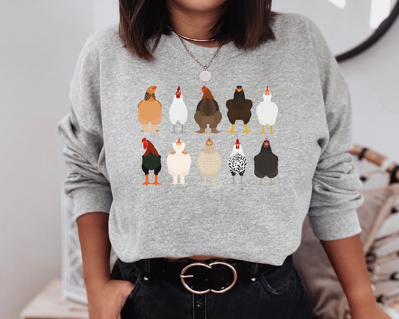 May include: A gray sweatshirt with a graphic print of 10 chickens in different colors and poses. The chickens are all facing forward and have their wings tucked in. The sweatshirt has long sleeves and a crew neck.