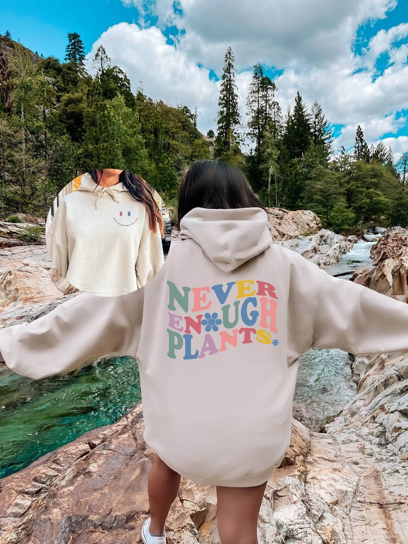 May include: A beige oversized hoodie with a colorful graphic on the back that says "NEVER ENOUGH PLANTS" with a flower in the middle of the word "ENOUGH".