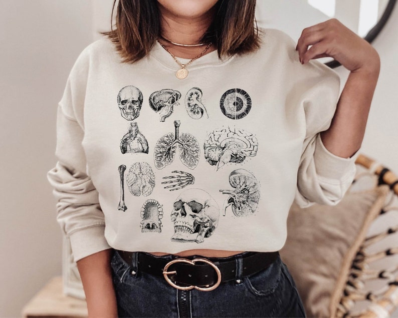 May include: A white cropped sweatshirt with a black anatomical illustration of various organs and a skull. The sweatshirt has a black belt with silver buckles.