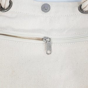 a close-up view of a zipper on a white fabric, with a metal zipper pull visible.
