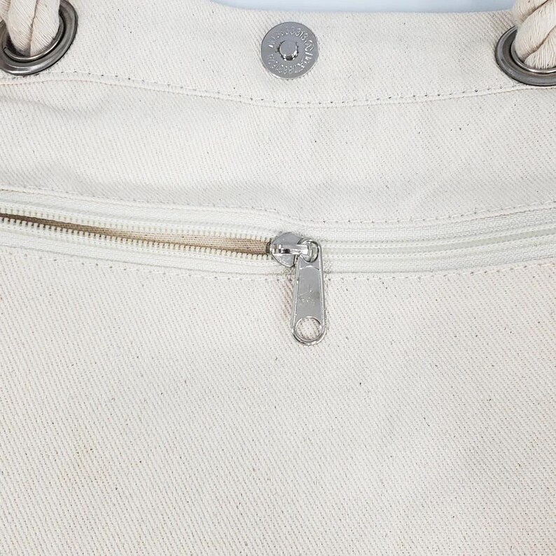 a close-up view of a zipper on a white fabric, with a metal zipper pull visible.