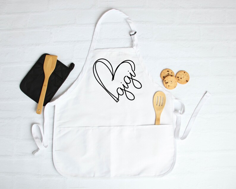 May include: White apron with a black heart and the word "Gigi" written inside. The apron has two pockets and adjustable straps.