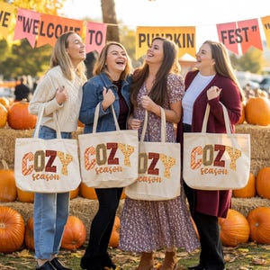 Four women standing in a row, each holding a tote bag with the word "COZY season" printed on it. They are smiling and appear to be enjoying themselves.