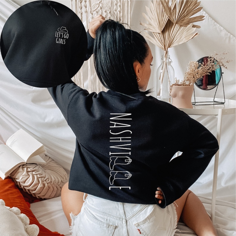May include: Black cropped sweatshirt with white text that reads "NASHVILLE" with a graphic of cowboy boots. The back of the sweatshirt has white text that reads "Let's go girls" with a graphic of a cowboy hat.