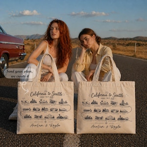 May include: Two beige tote bags with a black graphic of a road trip map from California to Seattle. The text "California to Seattle - Road Trip 2026" is printed on the bags. The bags are held by two people.
