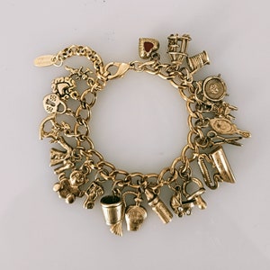 May include: Gold-coloured charm bracelet with a variety of charms, including a heart, sewing machine, thimble, perfume bottle, baby bottle, and a baby carriage. The bracelet has a lobster claw clasp and a chain link design. The charms are detailed and add a vintage aesthetic.