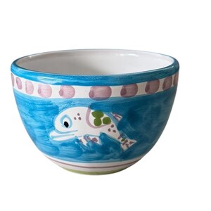 May include: A small, hand-painted ceramic bowl with a blue exterior. The bowl features a white fish design with green and pink accents. The rim has a pink and blue dotted pattern, and the base has a striped design.