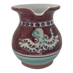 May include: A brown ceramic jug with a white octopus design. The jug has a blue and white band around the top and a blue and white stripe around the bottom.