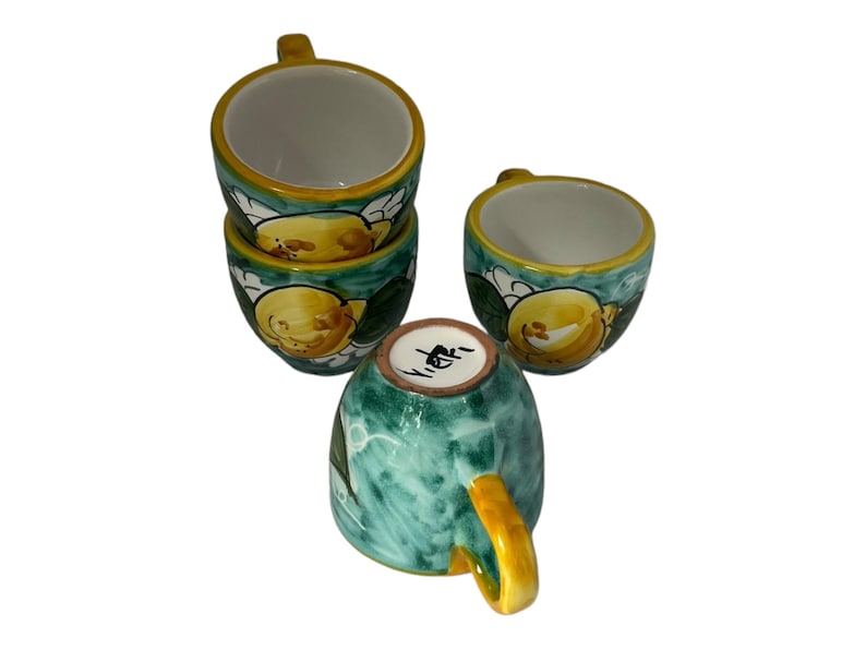Puede incluir: Juego de cuatro tazas de espresso de cer&aacute;mica con dise&ntilde;o de lim&oacute;n. Las tazas son verdes, amarillas y blancas con un dise&ntilde;o de lim&oacute;n pintado a mano. Las tazas est&aacute;n apiladas unas sobre otras.