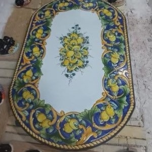 May include: Oval ceramic table top with a white background and a yellow lemon design. The border is blue and green with a rope design.