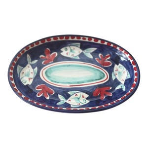 May include: An oval ceramic serving platter with a blue background and a white rim. The platter is decorated with red coral and white fish with black outlines.